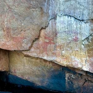 Red ochre pictograph of a moose on a textured rock cliff face in the Canadian wilderness.