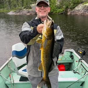 A happy fisherman in a boat holding a large golden Walleye caught on a remote Canadian lake.